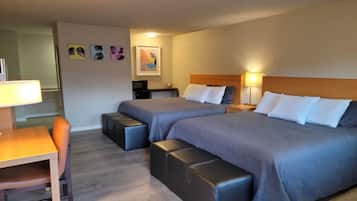 A hotel room with two beds, a desk, a chair, and a small kitchenette.