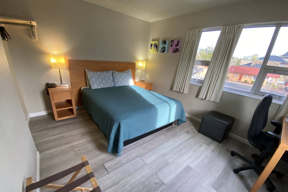 Une chambre à coucher comprenant un lit, des tables de chevet, un bureau, une chaise et une fenêtre avec des rideaux.