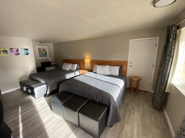 Habitación de hotel con dos camas, una mesita, un banco y una puerta.