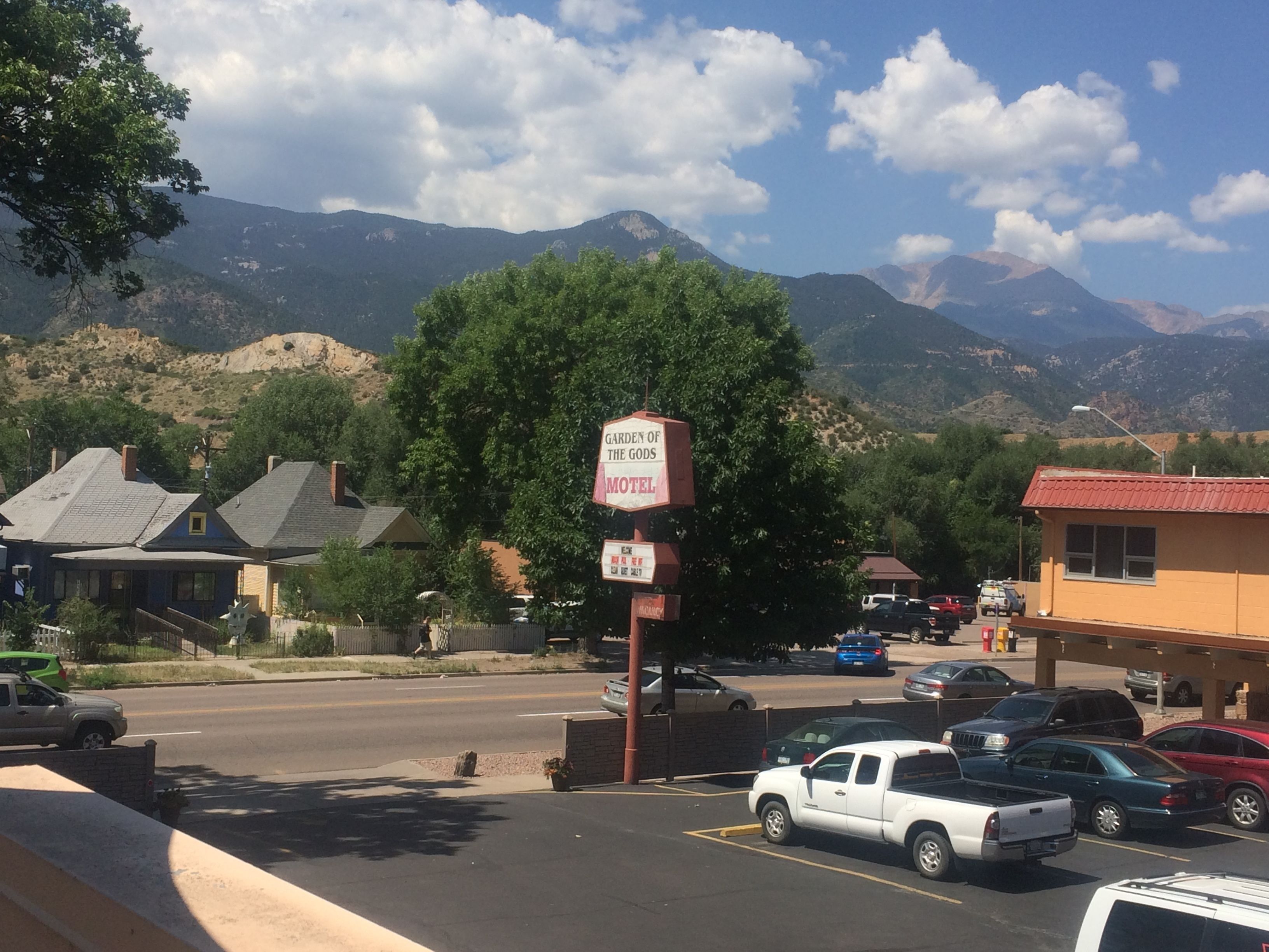 A motel with a sign reading "Garden of the Gods Motel" and a parking lot with several vehicles.
