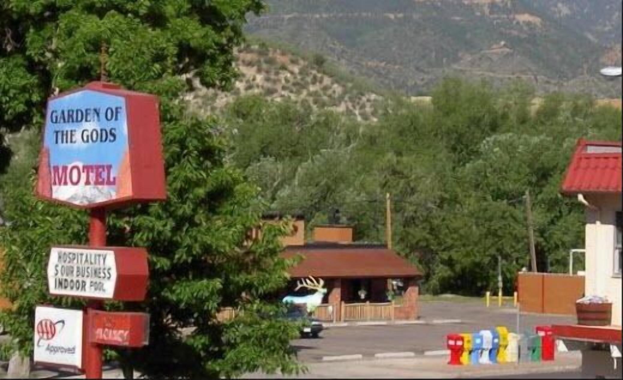 Letrero de motel con una placa que dice 'Garden of the Gods', un letrero de bienvenida y un sello de aprobación rojo.