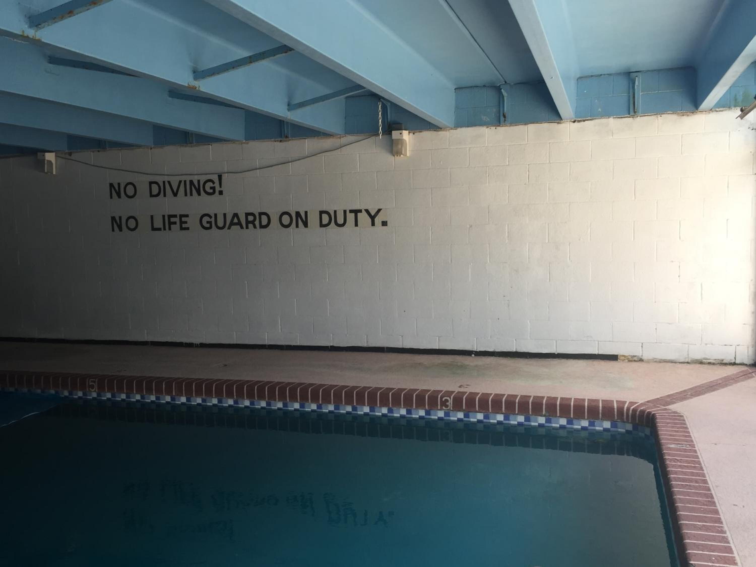 A swimming pool with a wall that has a warning sign stating 'NO DIVING. NO LIFE GUARD ON DUTY.'