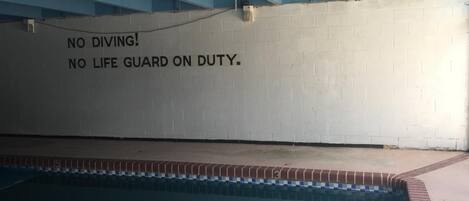 A swimming pool with a wall that has a warning sign stating 'NO DIVING. NO LIFE GUARD ON DUTY.'