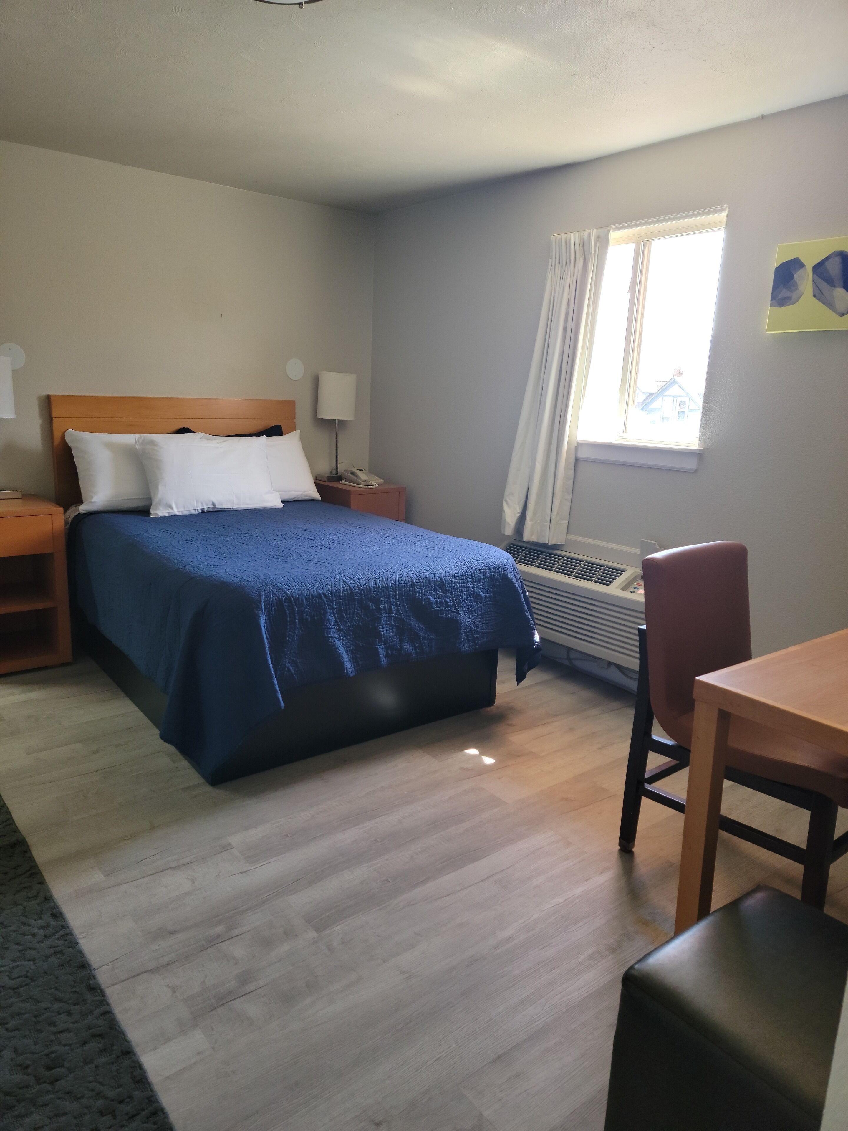 Ein Hotelzimmer mit Bett, Nachttisch, Lampe, Klimaanlage und einem Vorhangfenster.