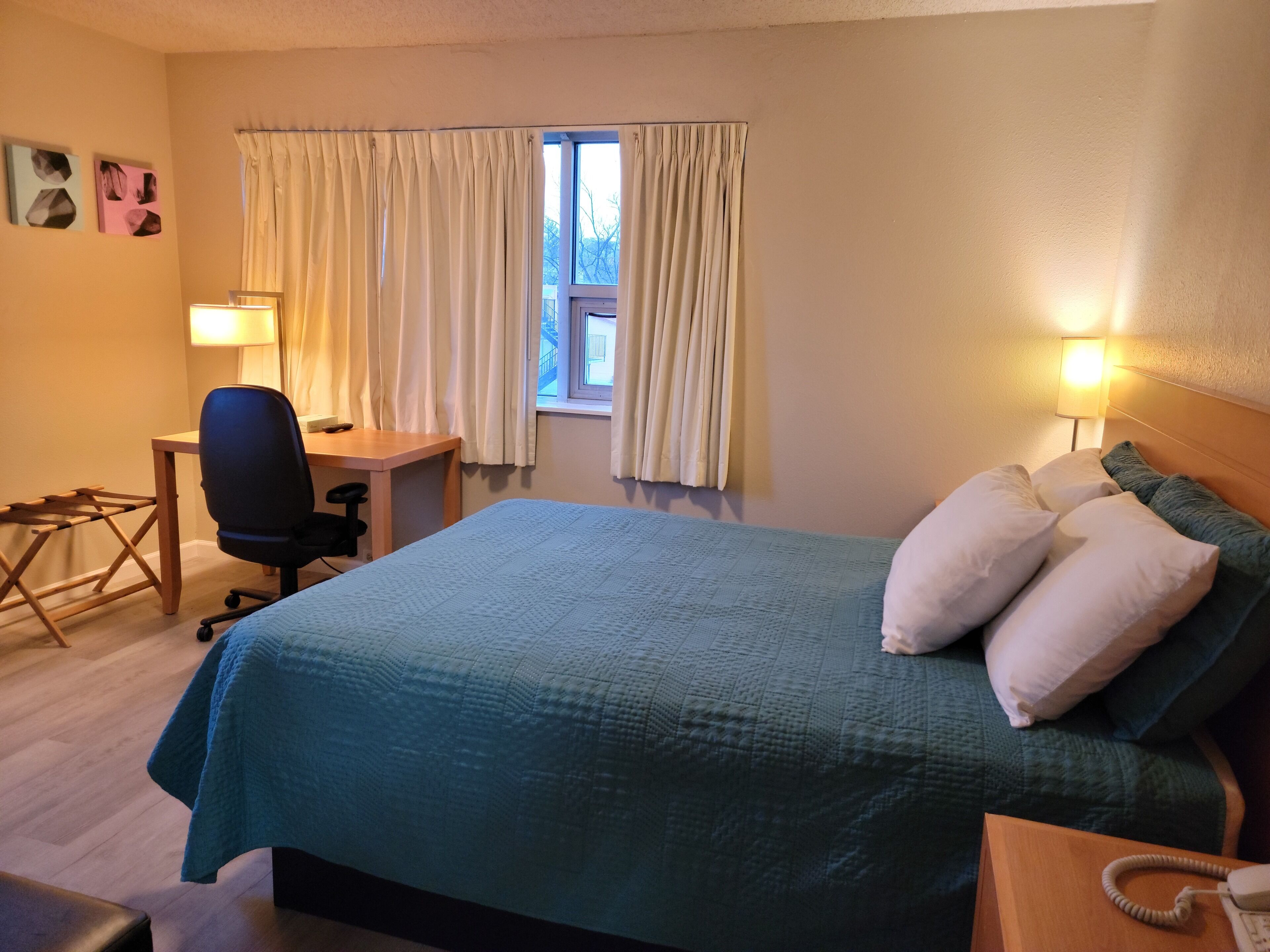 Une chambre d’hôtel bien aménagée, avec un lit, un bureau, une chaise et une fenêtre avec des rideaux.