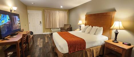 Una habitación de hotel con una cama grande, un escritorio con televisor, una silla, dos lámparas de noche y una puerta.