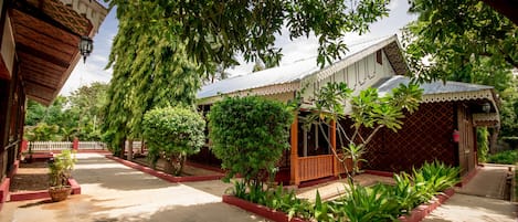 Un patio tradicional con un edificio de madera, una zona de estar cubierta y una gran variedad de plantas.