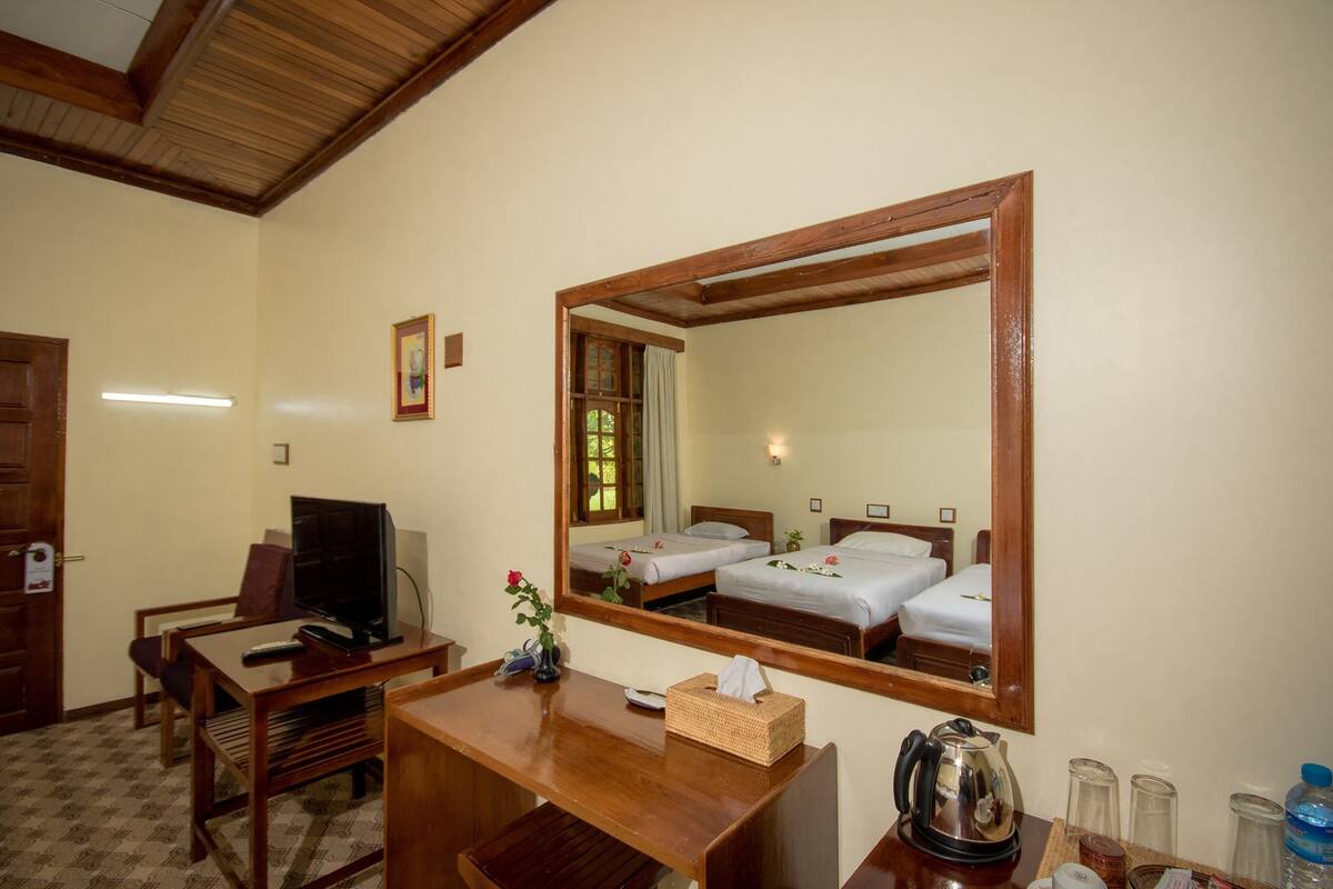 Habitación de hotel con un escritorio de madera, televisor, dos camas, un espejo grande y una ventana con cortinas.