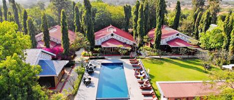 A resort with multiple red-roofed buildings, a central swimming pool, and lush greenery.