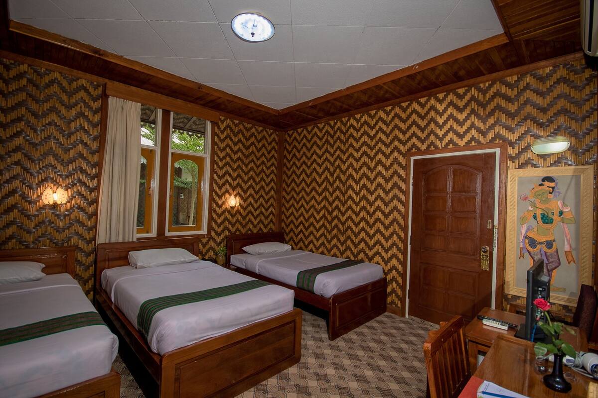 Habitación de hotel con tres camas de madera, un escritorio de madera, una silla, un espejo y una puerta.
