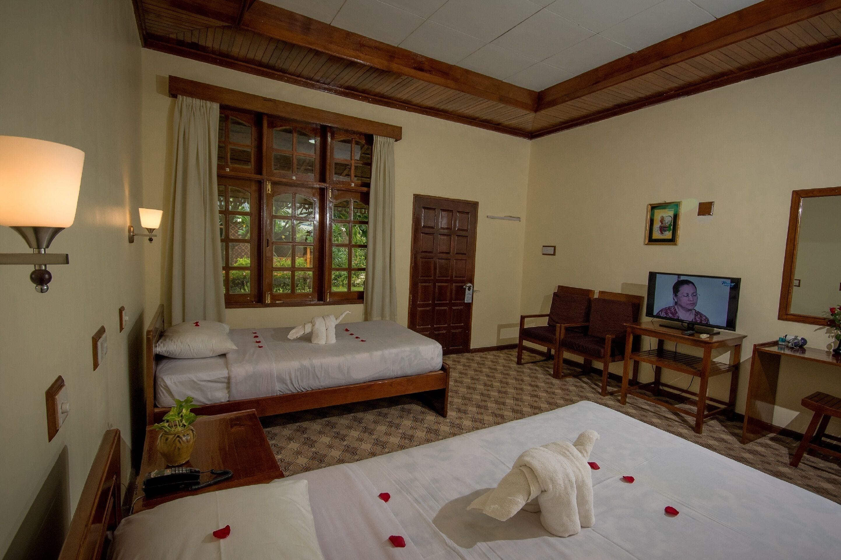 A hotel room with two beds, a television, a desk, and a large window.