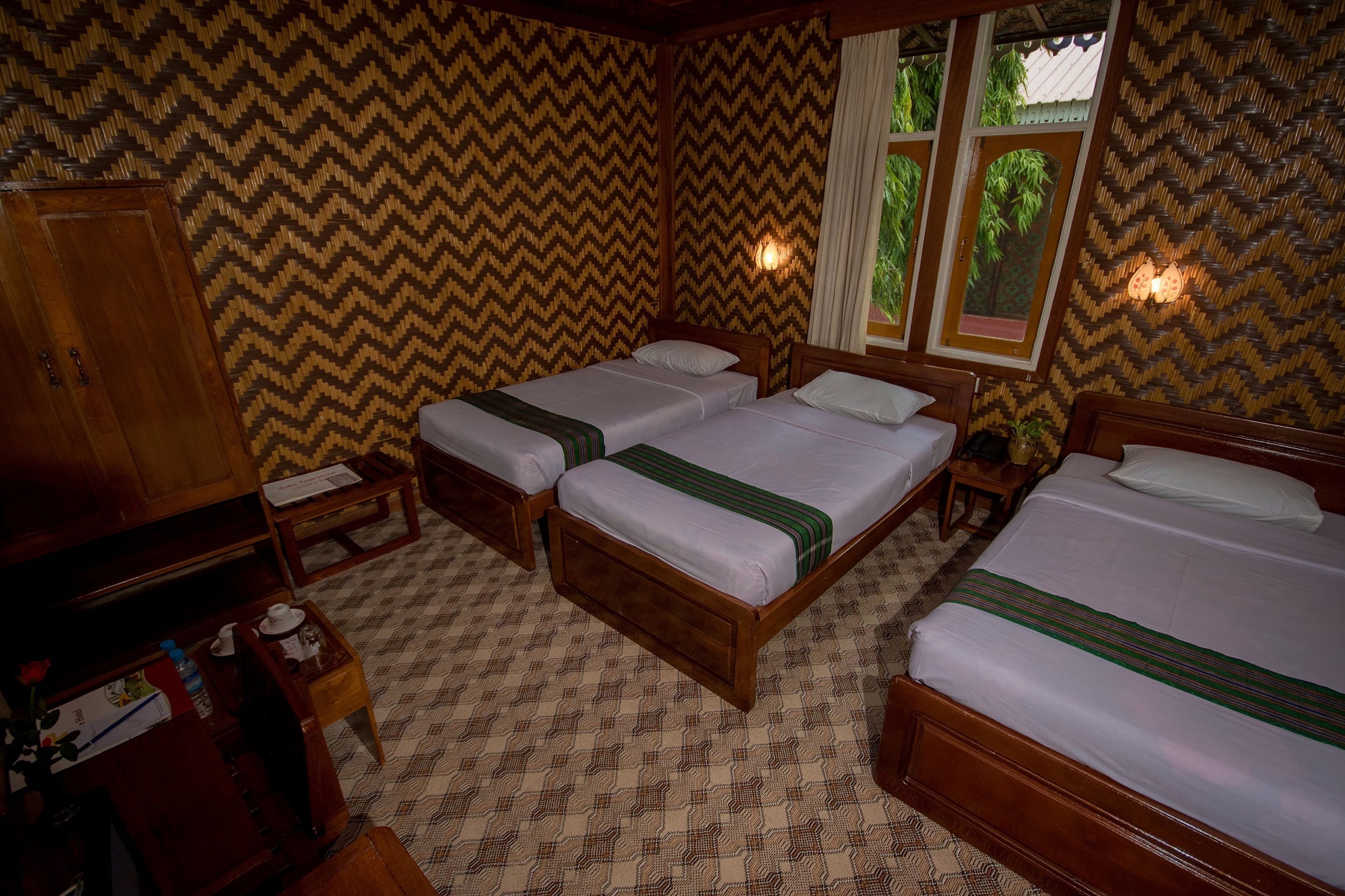 Une chambre avec deux lits en bois, une armoire en bois et une petite table avec une lampe.