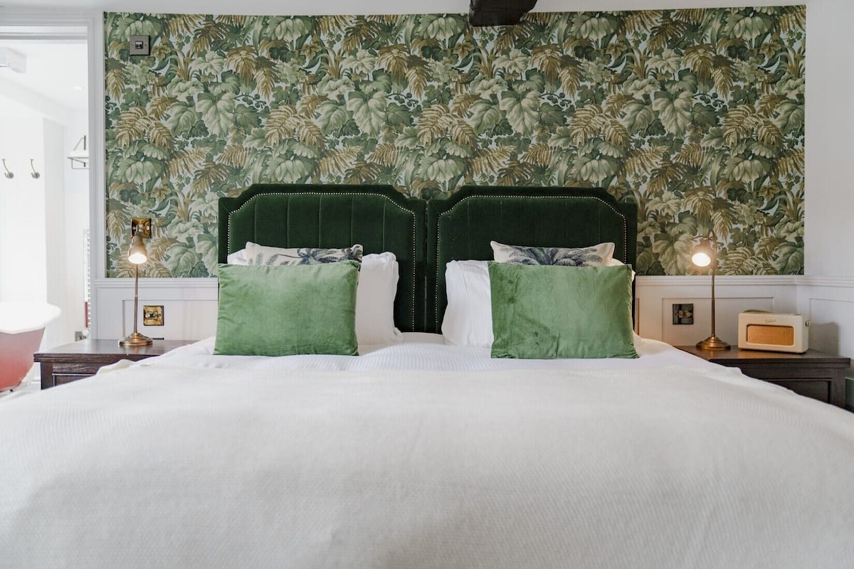 Una cama grande con cabecera tapizada en verde, dos almohadas verdes y ropa de cama blanca.