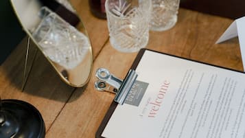 Une planche à découper avec une carte de bienvenue, un plateau en métal avec un verre et un chandelier sur une table en bois.