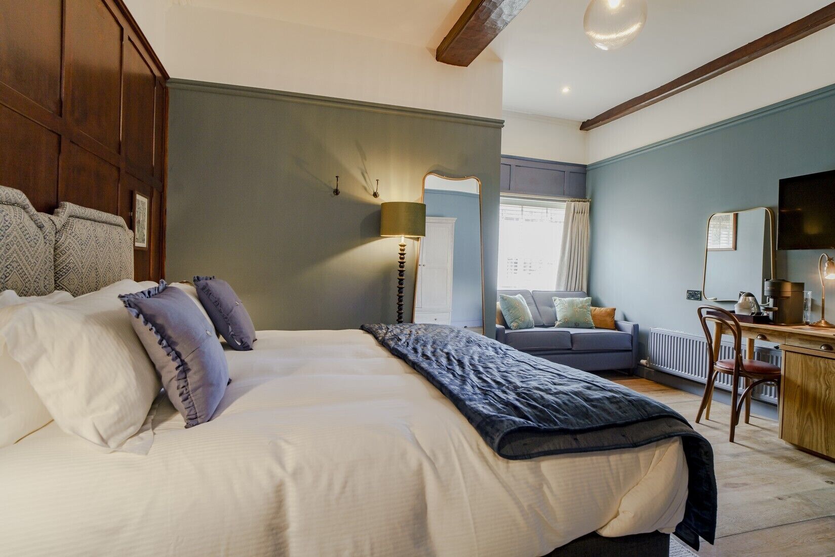 Une chambre à coucher comprenant un lit, un bureau, une chaise, une lampe, un miroir et une fenêtre avec des rideaux.