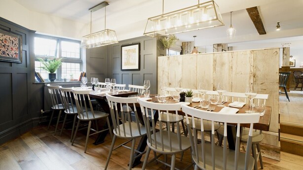 Un comedor con mesas y sillas redondas, lámparas colgantes y un panel de madera.