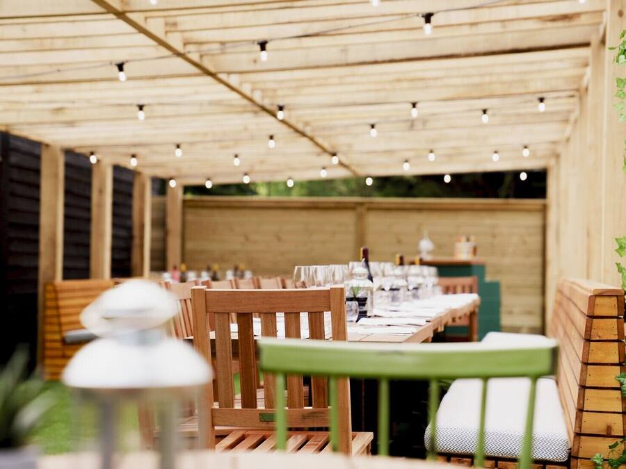 Un área de comedor al aire libre con mesas y sillas de madera, luces colgantes y techo de madera.