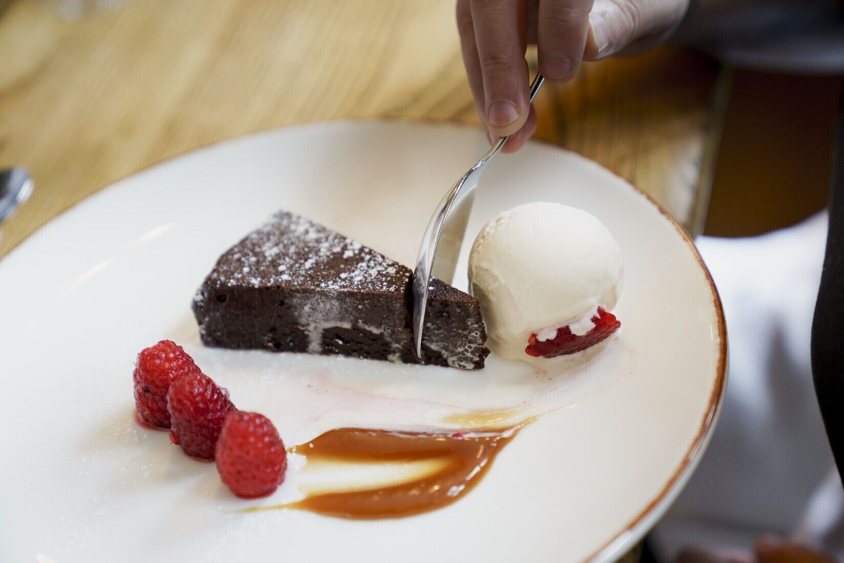 Un plato de postre con una porción de pastel de chocolate, una bola de helado de vainilla y frambuesas frescas.