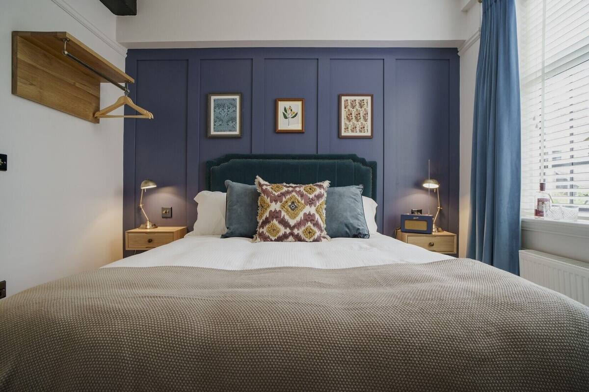 Un dormitorio con una cama, dos mesitas de noche, un estante de madera y tres láminas enmarcadas con motivos botánicos en la pared.