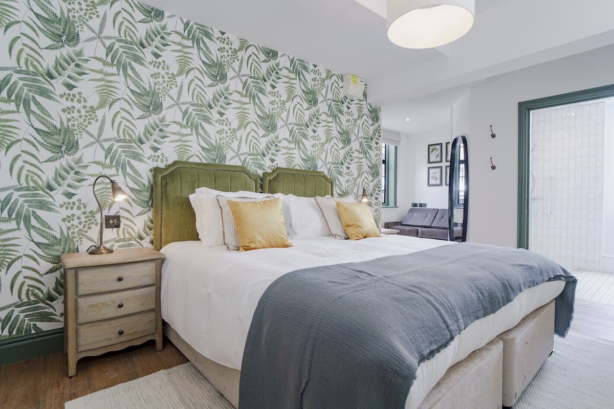 Un dormitorio moderno con una cama grande, una mesita de noche, una lámpara y un cabecero verde.
