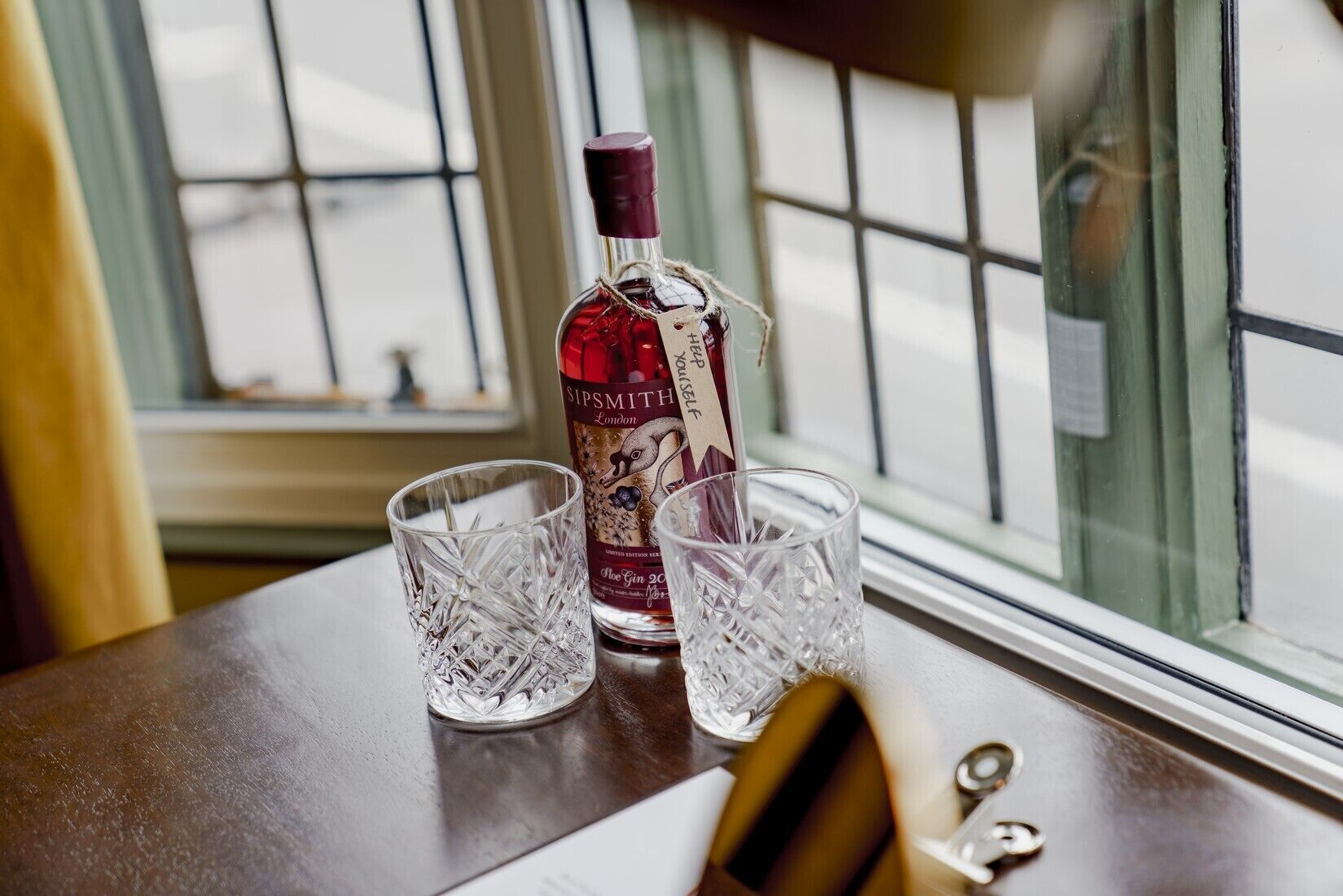 Una botella de ginebra Sipsmith London y dos vasos sobre una mesa junto a una ventana.