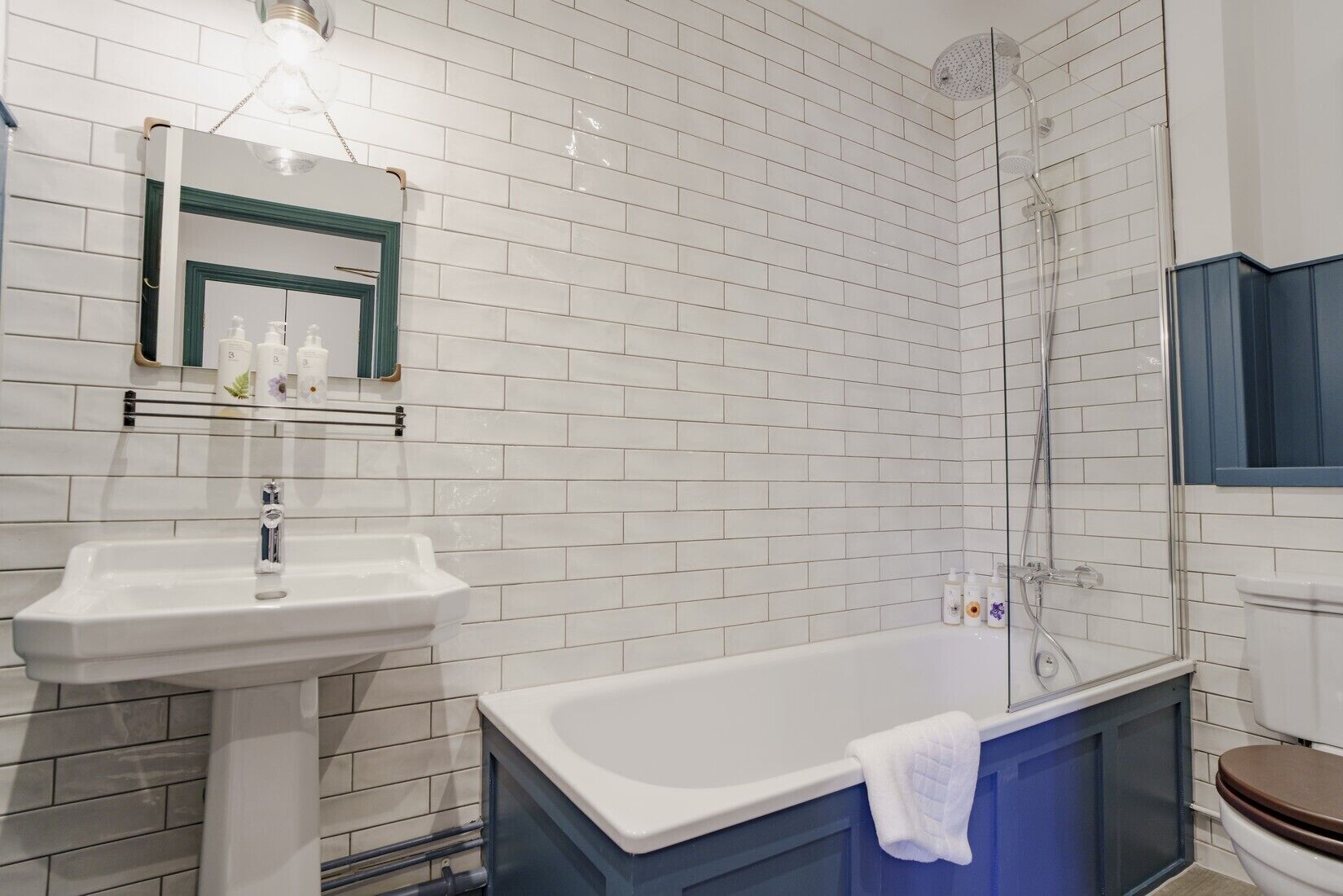 A bathroom with white tiled walls, a white sink, a blue bathtub, and a toilet.