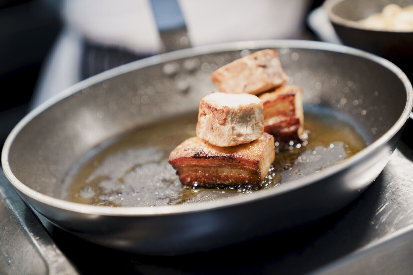 A frying pan with pieces of meat cooking in oil.