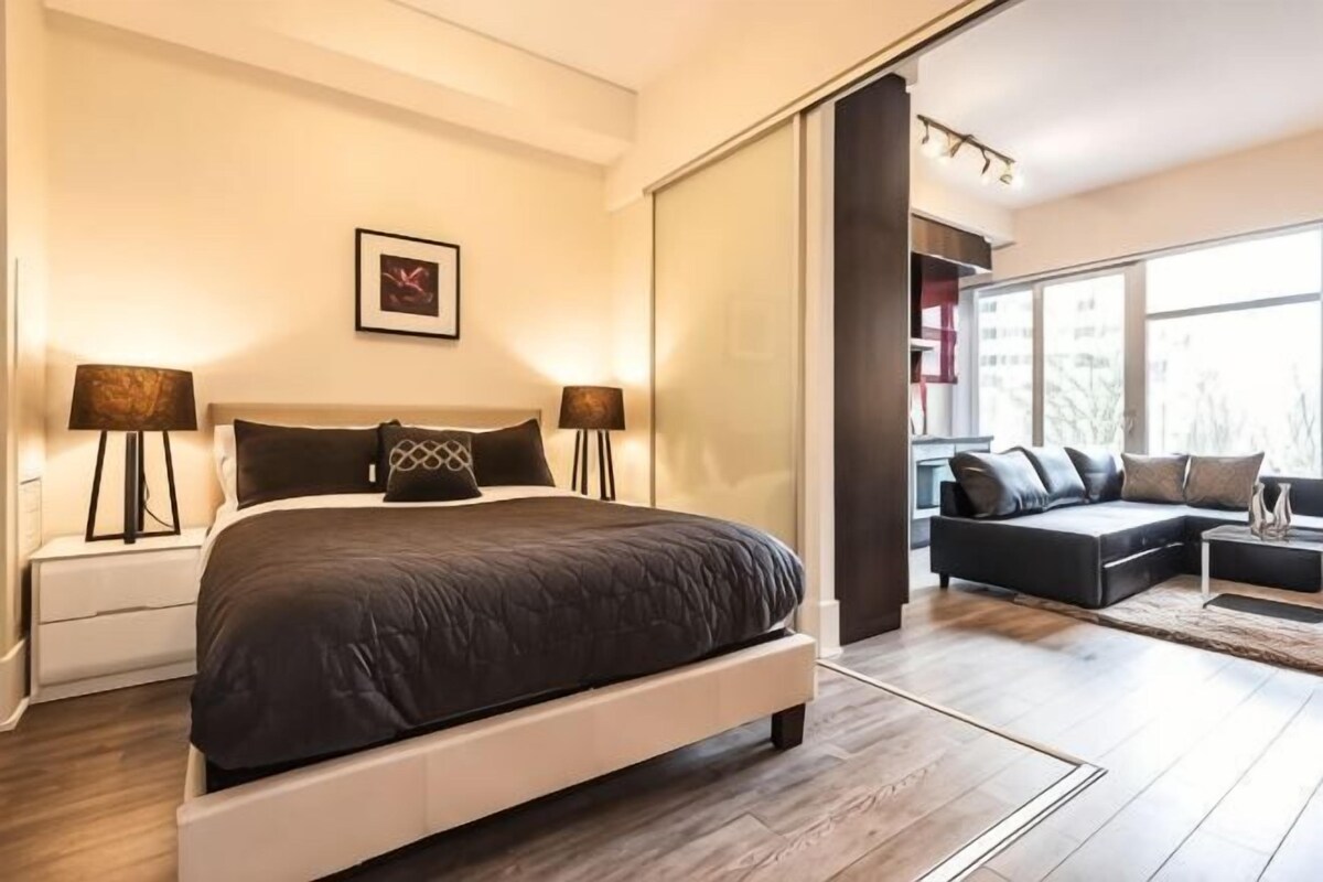 Un dormitorio con una cama grande, lámparas de noche, un sofá y una puerta corredera a una sala de estar.