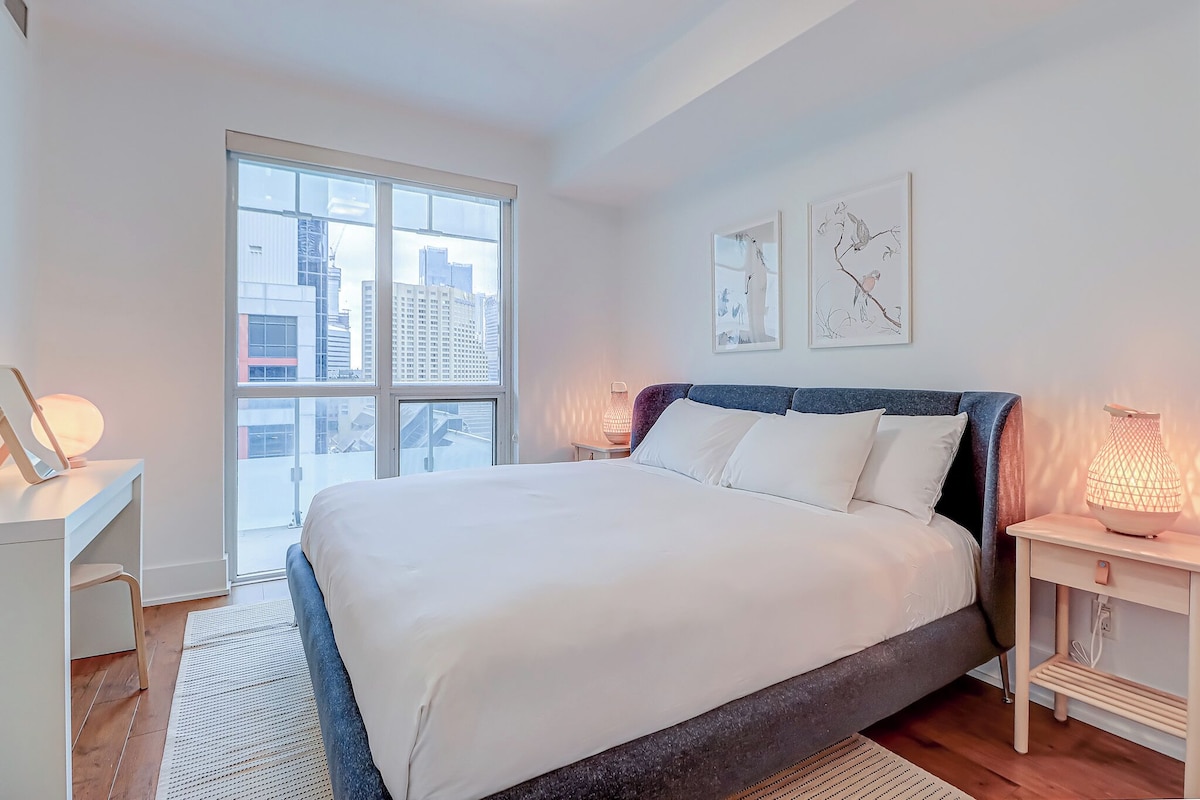 Un dormitorio moderno con una cama grande, un escritorio y una ventana con vista a la ciudad.