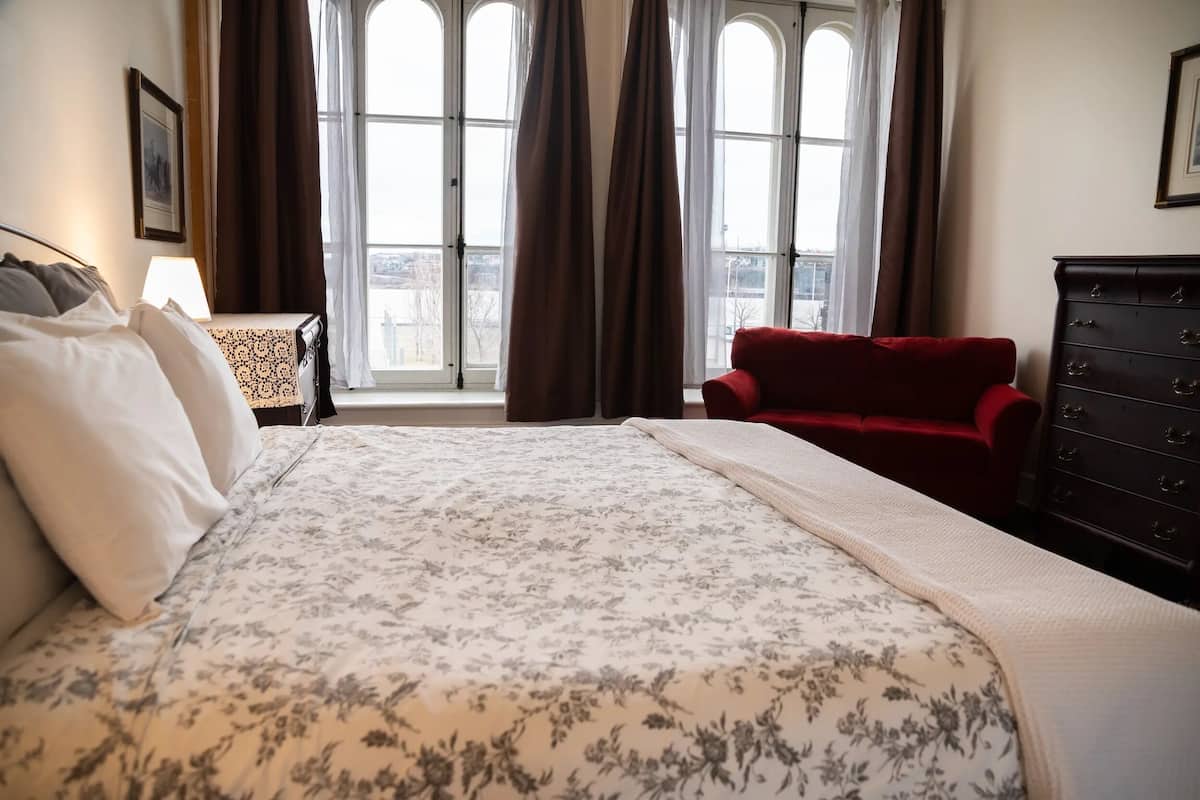 A hotel room with a large bed, a red sofa, a dresser, and a window with curtains.