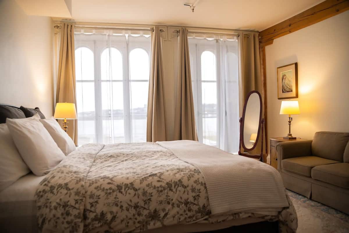 A hotel room with a large bed, two bedside lamps, a mirror, a sofa, and a window with curtains.