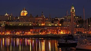 A nighttime cityscape with illuminated buildings and a marina with boats. - Royal Dalhousie Condos (Québec City)