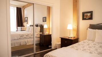A hotel room with a mirrored closet, a bed with a floral bedspread, a bedside table with a lamp, and a small bedside table with a lamp.