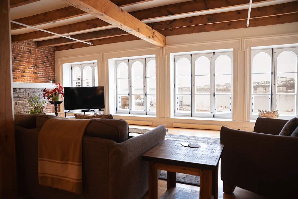 A cozy living room with a fireplace, large windows, and a TV.