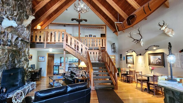 A spacious living area with a stone wall, a black leather sofa, a wooden staircase, and a dining area with wooden furniture. - Nisqually Lodge (Ashford)