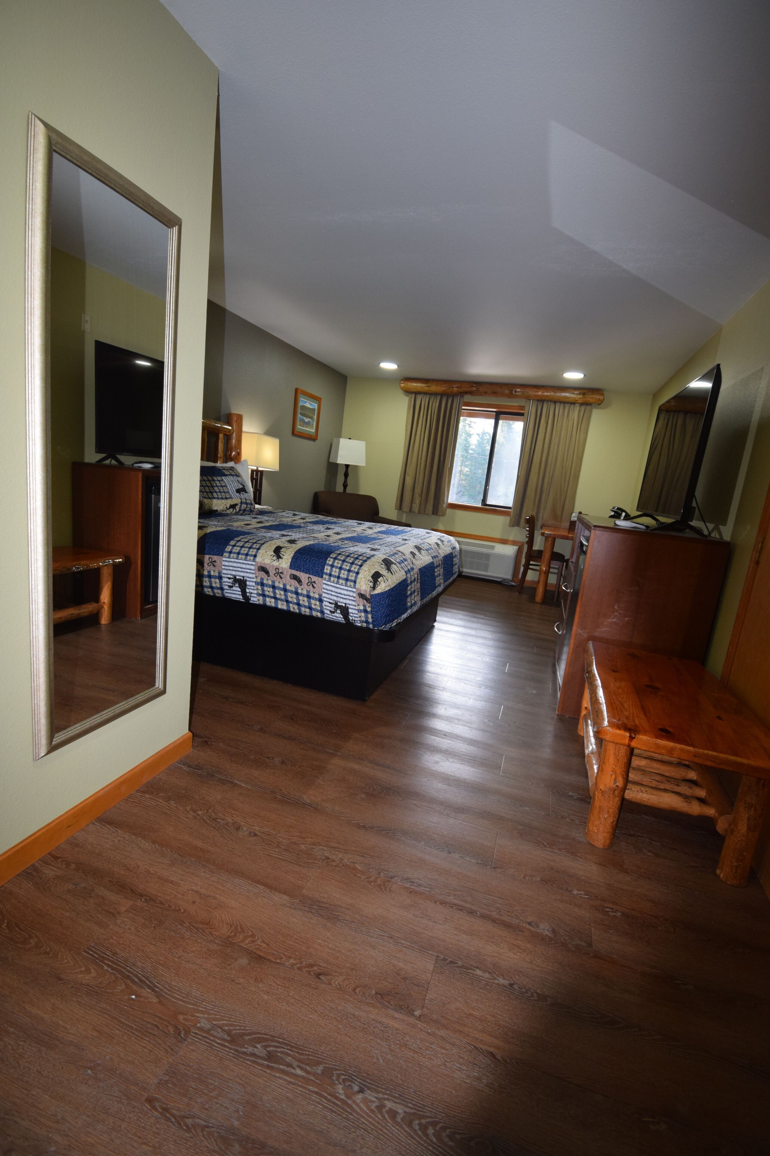 A bedroom with a bed, a desk, a chair, a television, and a window.
