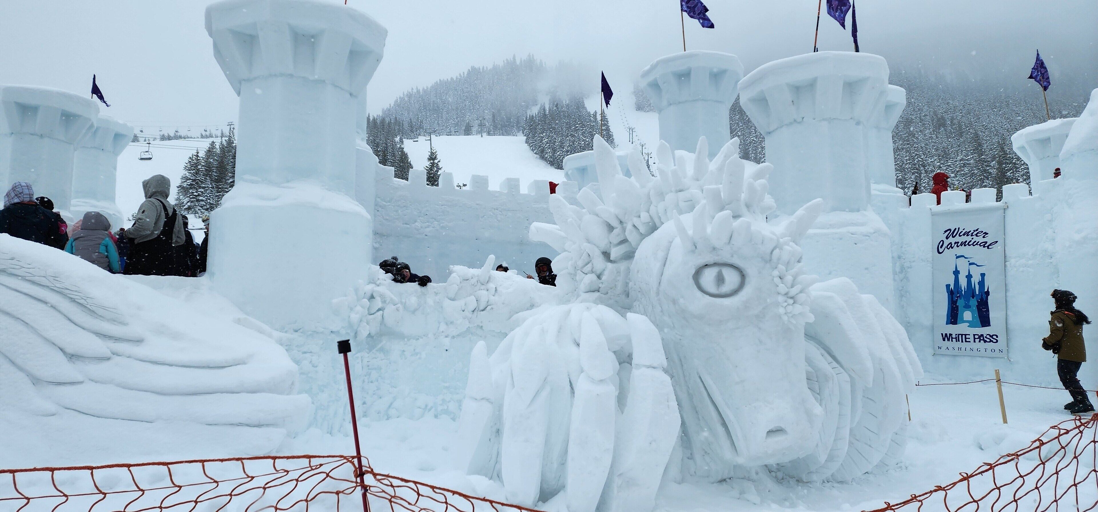 Eine Schneeskulptur mit Burg und Pferd, umgeben von einem Zaun.
