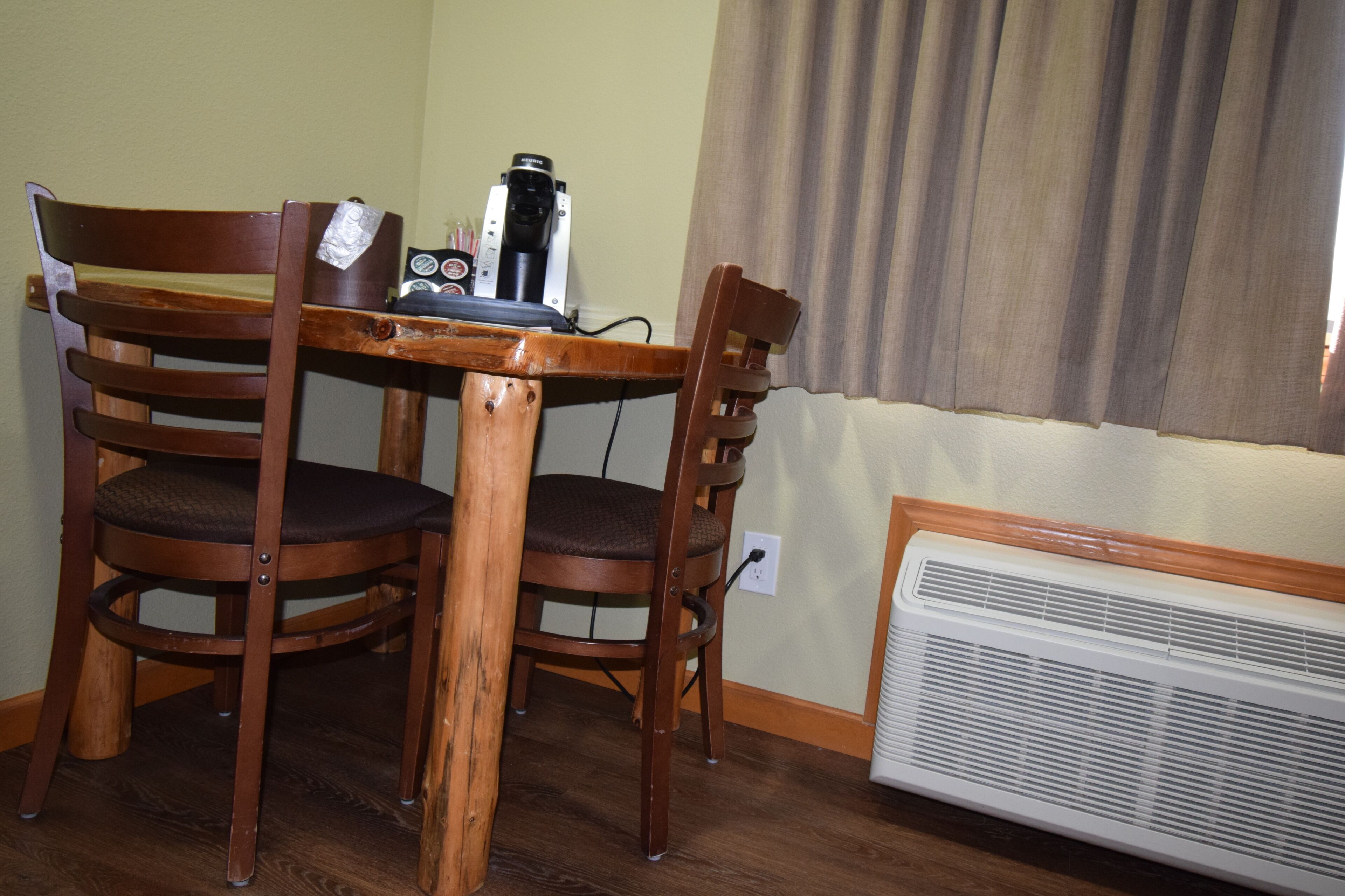 A dining area with a wooden table and chairs, a coffee maker, and a wall-mounted heater.