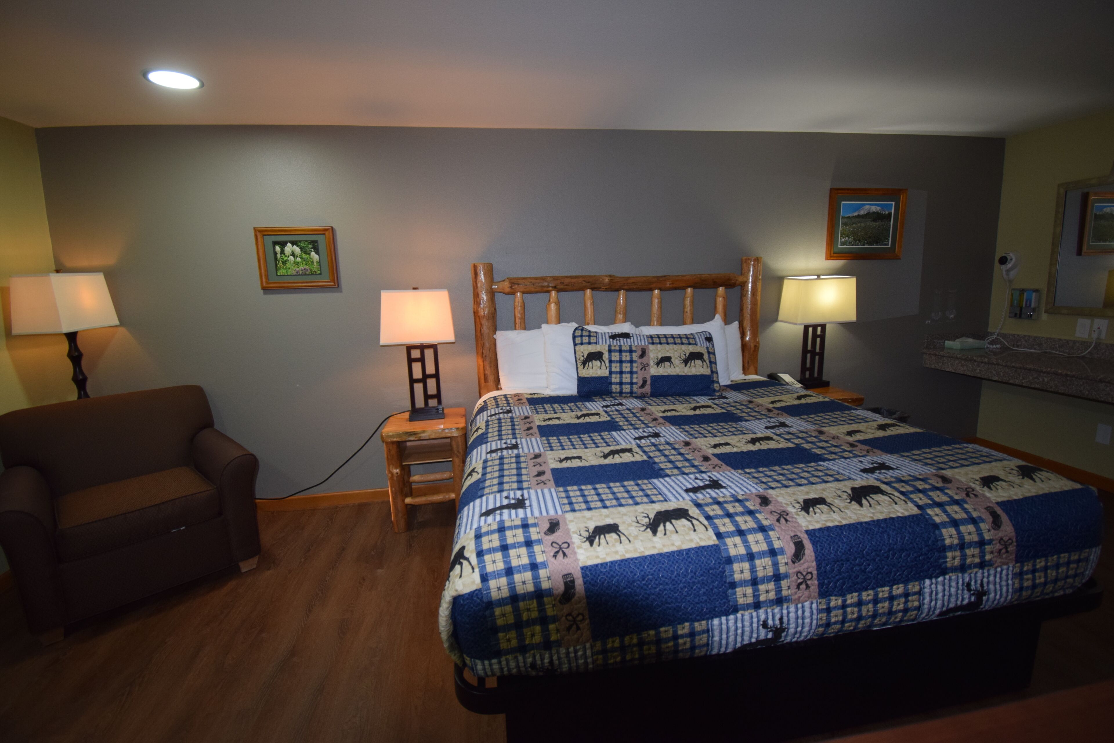 A bedroom with a bed, two bedside lamps, a nightstand, a chair, and framed pictures on the wall.