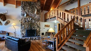 A rustic interior with a stone fireplace, a leather sofa, a wooden staircase, and mounted animal heads. - Nisqually Lodge (Ashford)