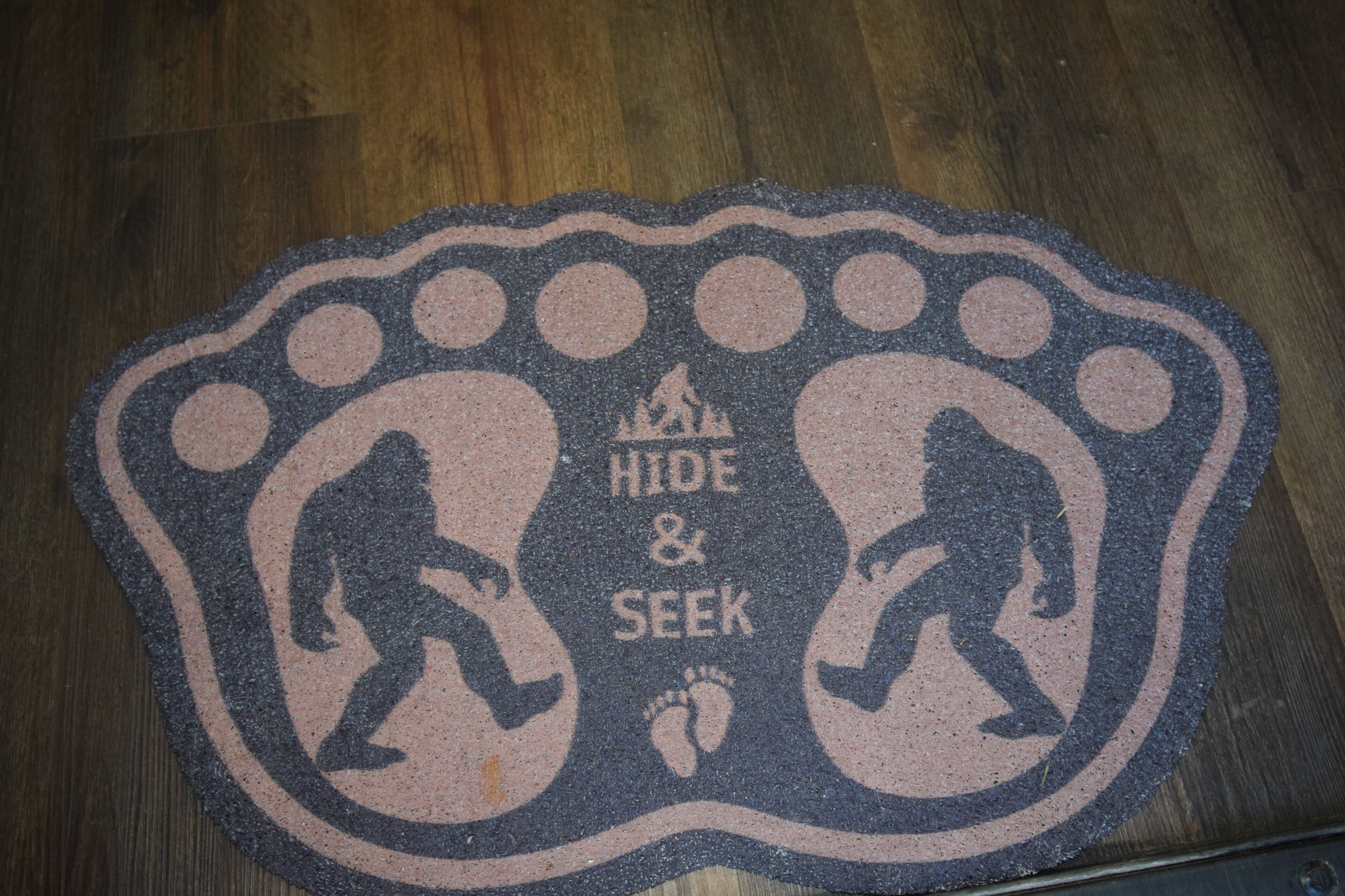 A doormat with footprints and the words 'HIDE & SEEK' in a circular pattern.