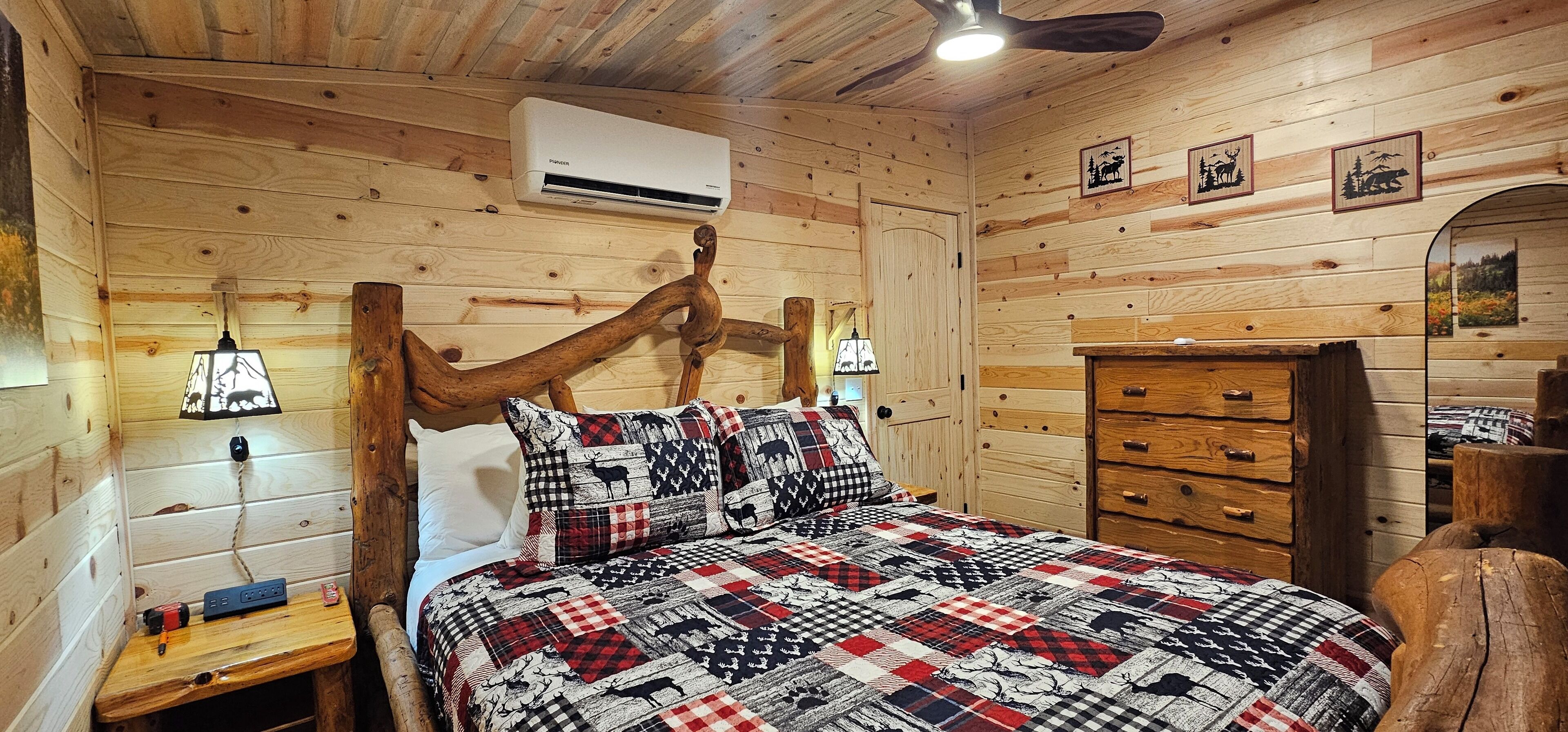 Un dormitorio de cabaña de madera acogedor, con cama, mesita de noche, cómoda y ventilador de techo.