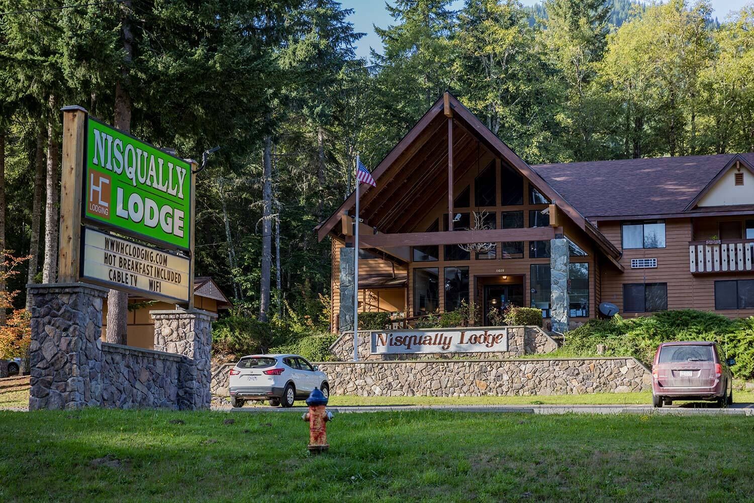 Una cabaña con un letrero visible, paredes de piedra y un edificio grande de madera con techo a dos aguas.