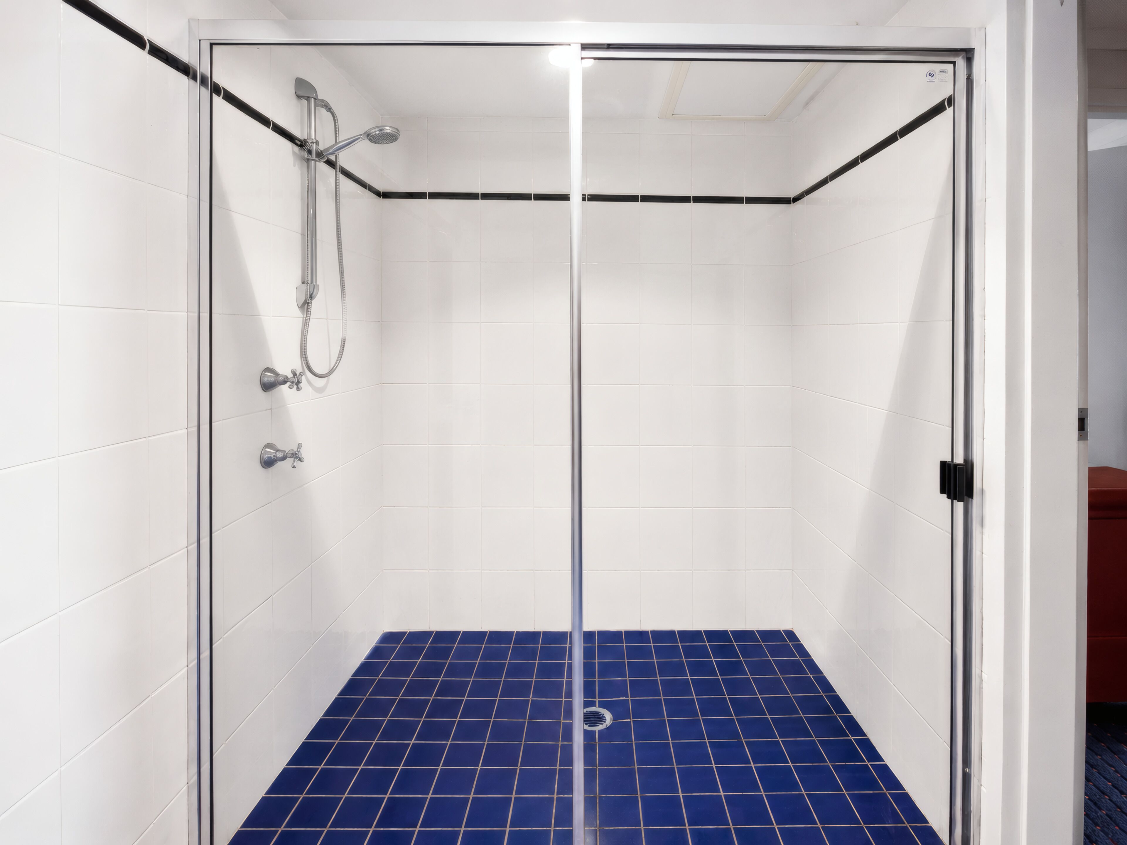 A glass-enclosed shower with white tiled walls and a blue-tiled floor.