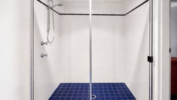 A glass-enclosed shower with white tiled walls and a blue-tiled floor.
