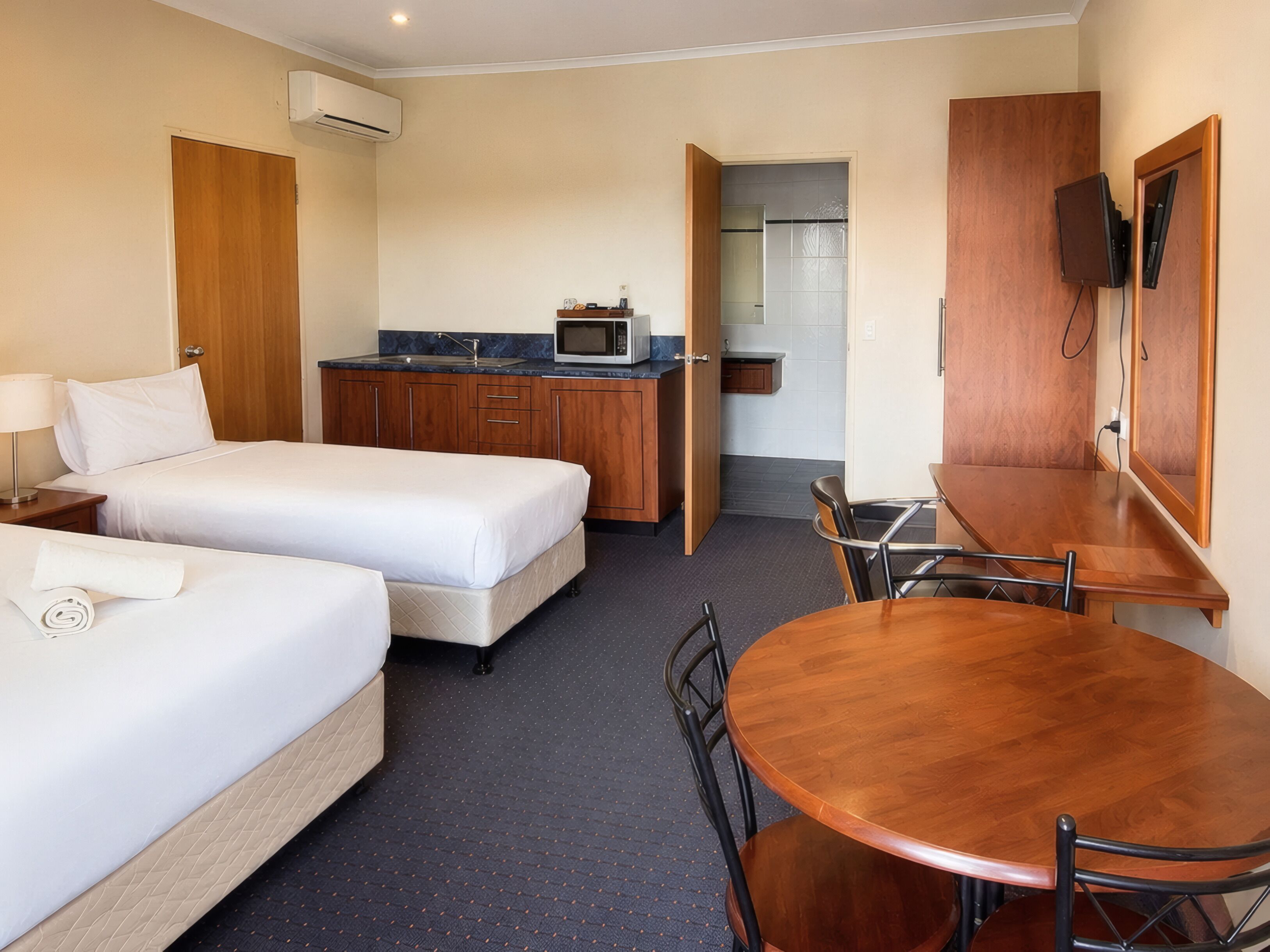 Een hotelkamer met twee bedden, een kitchenette, een eettafel met stoelen en een aan de muur bevestigde televisie.