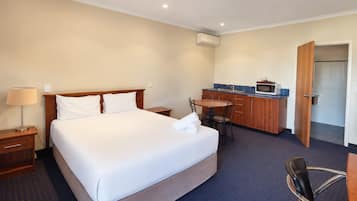 Een hotelkamer met een bed, nachtkastje, lamp, een kitchenette met een magnetron, en een badkamers deur.