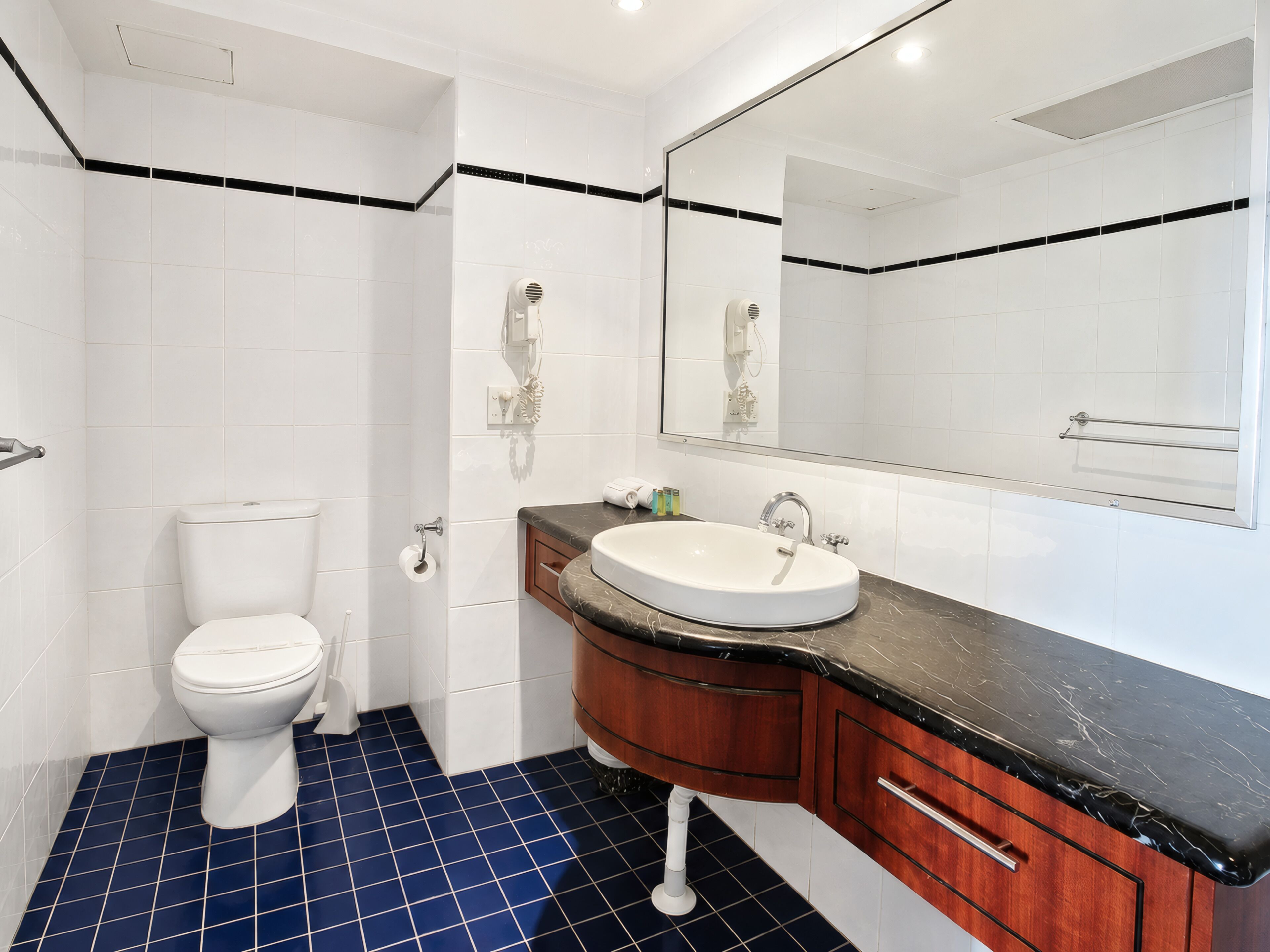 Une salle de bain avec des toilettes blanches, un lavabo doté d’un plan-vasque noir et un miroir au-dessus du lavabo.
