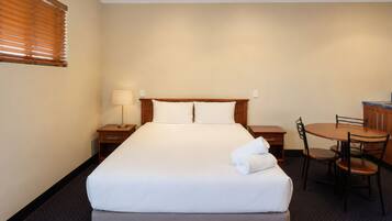Habitación de hotel con cama, mesita de noche con lámpara, una silla y una pequeña mesa con otra silla.