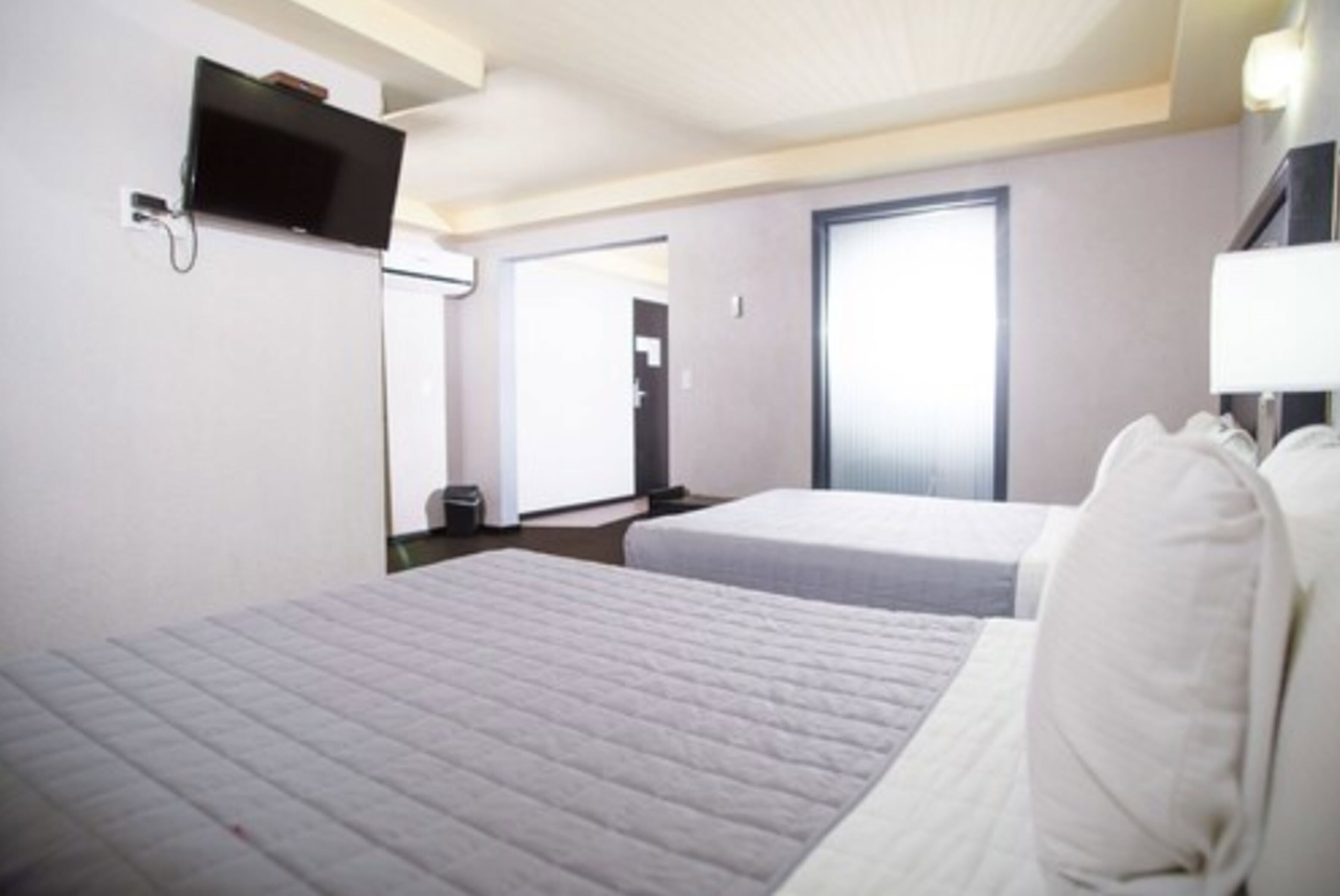 Habitación de hotel con dos camas, un televisor montado en la pared, una puerta y una ventana.